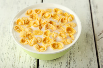 Bowl of cornflakes with milk on white wooden background