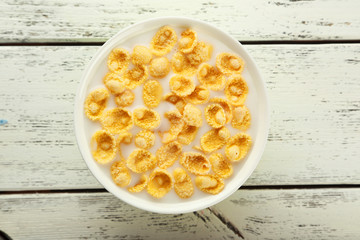 Bowl of cornflakes with milk on white wooden background