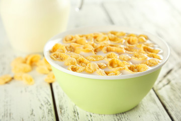 Bowl of cornflakes with milk on white wooden background