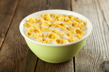 Bowl of cornflakes with milk on brown wooden background