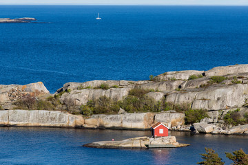Obraz premium Pretty small red cabin on a tiny island with a sailing boat in t