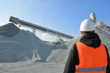 Worker and heavy machine for gravel production in background - obrazy, fototapety, plakaty