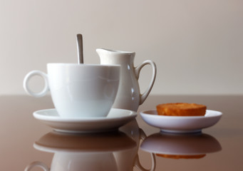 Cup of coffee, creamer jug and muffin on reflective table