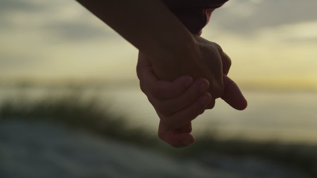 Couple holding hands at the beach at sunset in slow motion