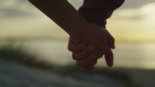 Unseen couple holding hands at the beach at sunset