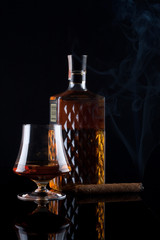 glass of brandy and bottle with smoking cigar