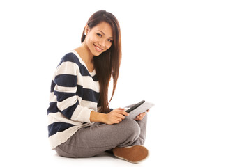 Smiling asian girl with tablet pc is sitting on the floor over w