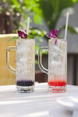 A glass of Sweet soda filled with ice cubes, soda and orchid flo