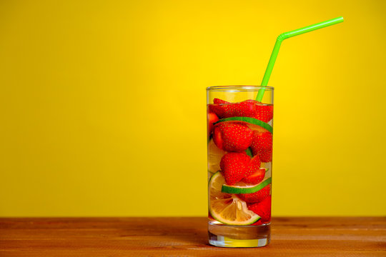 Glass of water with lime and strawberry on yellow background  