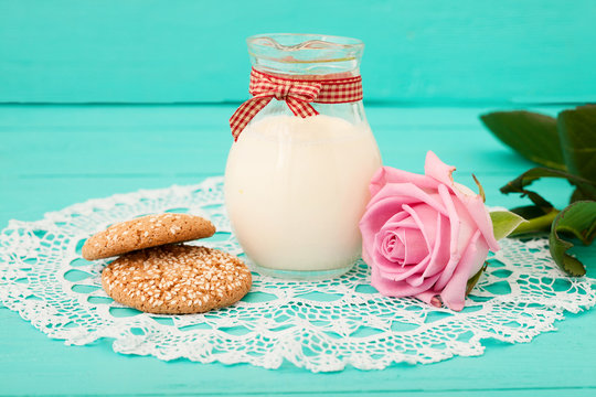 Breakfast with a jug of milk and cookies. Pink rose and lace napkin on wooden table.