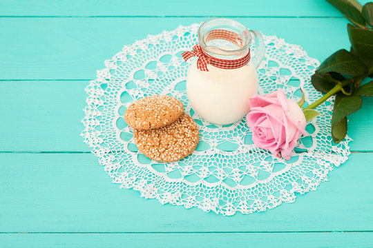Breakfast with jug of milk and cookies near rose on lace napkin. Wooden background
