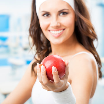Happy woman giving red apple, at fitness center