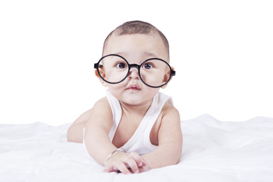 Baby boy with glasses lying on bed