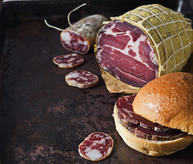 Cured pork shoulder with salami over black metal surface.