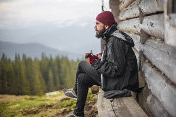 bearded guy playing guitar in mountains near wooden house