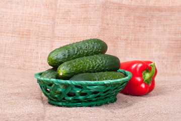 A bunch of cucumbers in a wicker basket, rear red pepper, burlap
