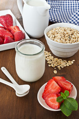 Greek yogurt in a glass jars with strawberry on  old wooden surface.