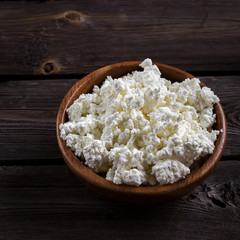 Cottage cheese in a bowl on wooden table. Style rustic.