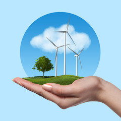 Fototapeta na wymiar Wind turbines with tree in female hand against blue sky