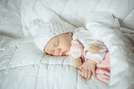 sweet small baby sleeps with a toy cat in a white hat