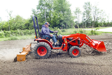 Older Gentleman Tilling His Garden With A Compact Tractor