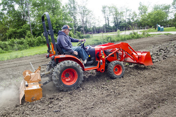 Elderly Man Tilling His Garden With Small Tractor