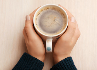 Female hands holding cup of coffee on wooden background