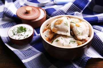 Tasty dumplings with fried onion in brown bowl, on wooden background