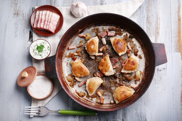 Fried dumplings with onion and bacon in frying pan, on wooden table background