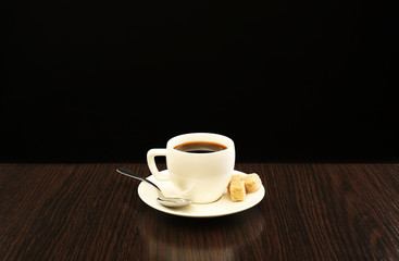 Cup of coffee with lump sugar on wooden table, on dark background