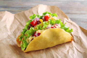 Tasty taco with vegetables on paper close up