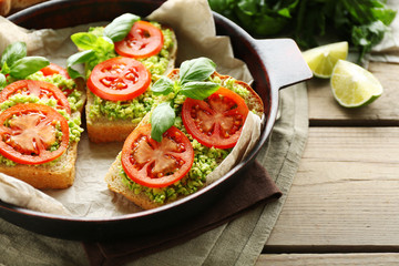 Vegan sandwich with avocado and vegetables on pan, on wooden background