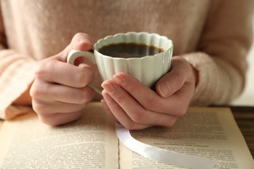 Woman holding cup of coffee and read the book, close up