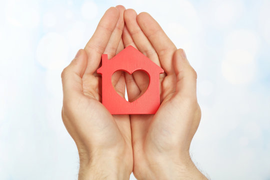 Female hands holding house on light blurred background