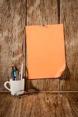 orange paper with pencil in a cup on wood background