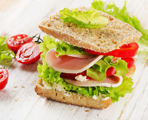 Sandwich with turkey and fresh vegetables on  a wooden table
