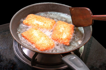 breaded chicken pieces being deep fried in a cast iron pan