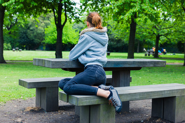 Naklejka na ściany i meble Young woman sitting on bench by table in park