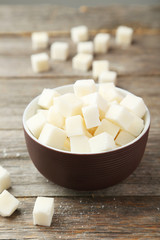 Fototapeta na wymiar Sugar cubes in bowl on grey wooden background