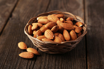 Almonds in basket on brown wooden background