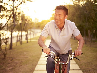 asian man enjoying bike riding outdoor in park at sunset - Powered by Adobe