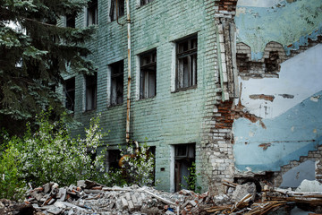 Fototapeta na wymiar Ruined abandoned green bricks building with windows and fir tree