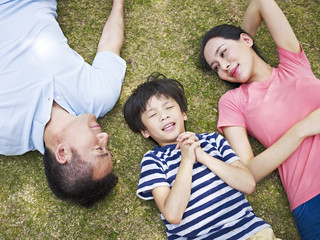 child lying on grass making a wish as parents watching