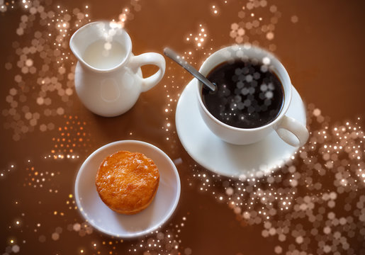 Cup of coffee, creamer jug and muffin on reflective table