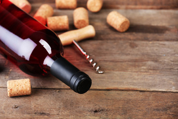 Glass bottle of wine with corks and corkscrew on wooden table background