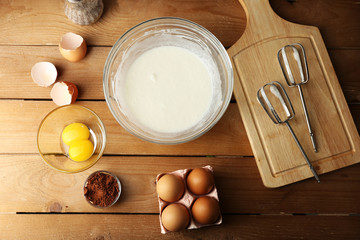 Preparation cream with eggs in glass bowl on wooden table, top view