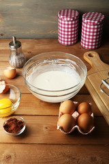 Preparation cream with eggs in glass bowl on wooden background