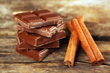 Pieces of chocolate with cinnamon sticks on wooden background