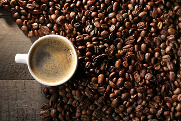 Cup of coffee with grains on wooden table, top view