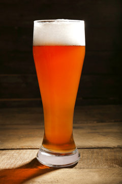 Glass of beer on wooden table on dark background